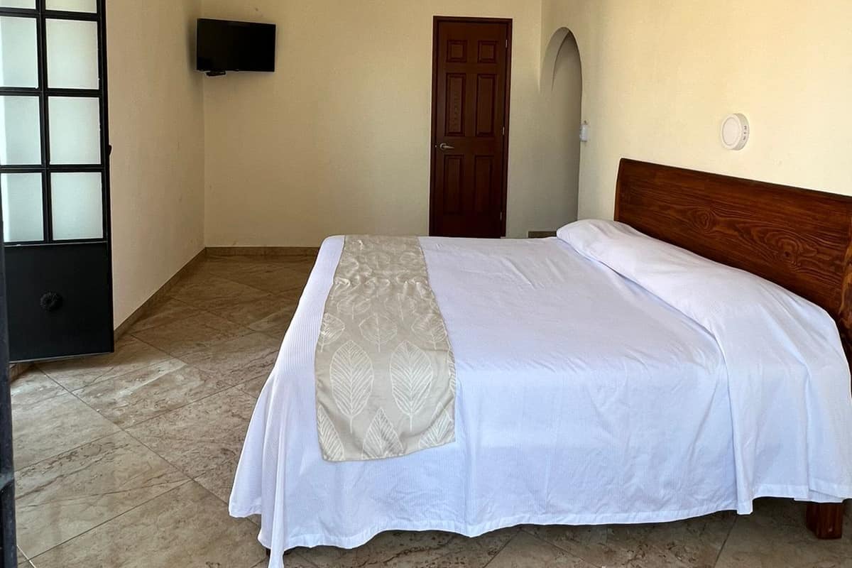 Un dormitorio con una cama, televisión en la pared, una puerta y suelo de baldosas.