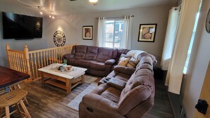 A cozy living room with a brown leather sofa, wooden coffee table, and a TV mounted on the wall. - Stage Stop Suite (Piedmont)