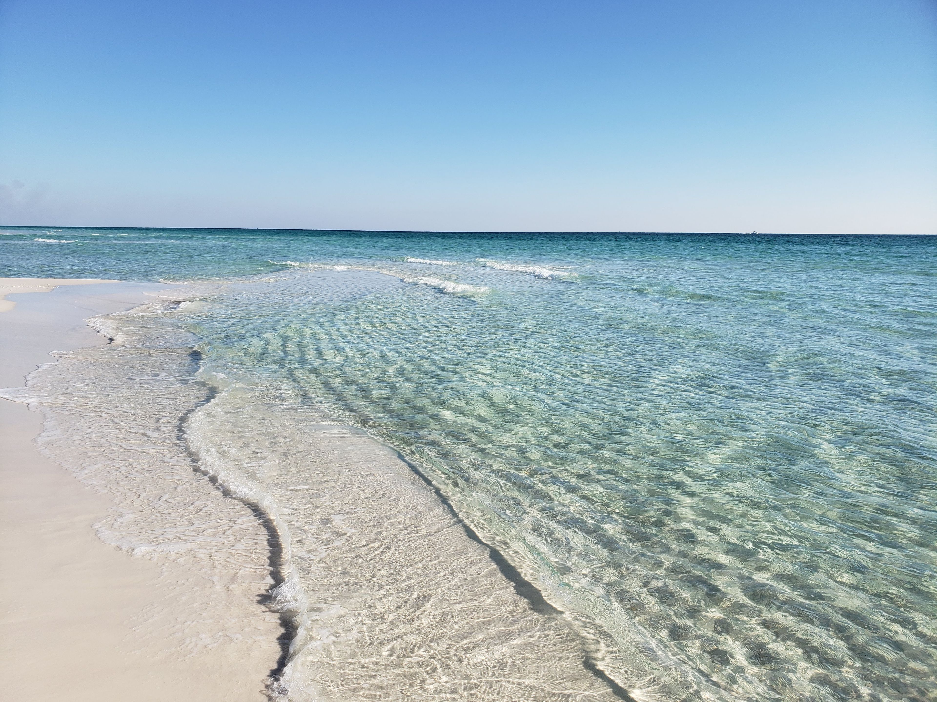 A beach with clear shallow waters and a sandy shore.