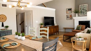 A living room with a dining table, chairs, a sofa, a television, and a fireplace. - Destin Townhome Steps from Beach & Pool (Destin)