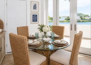 Un coin repas avec des chaises en osier, une table en verre et une vue sur l’eau.