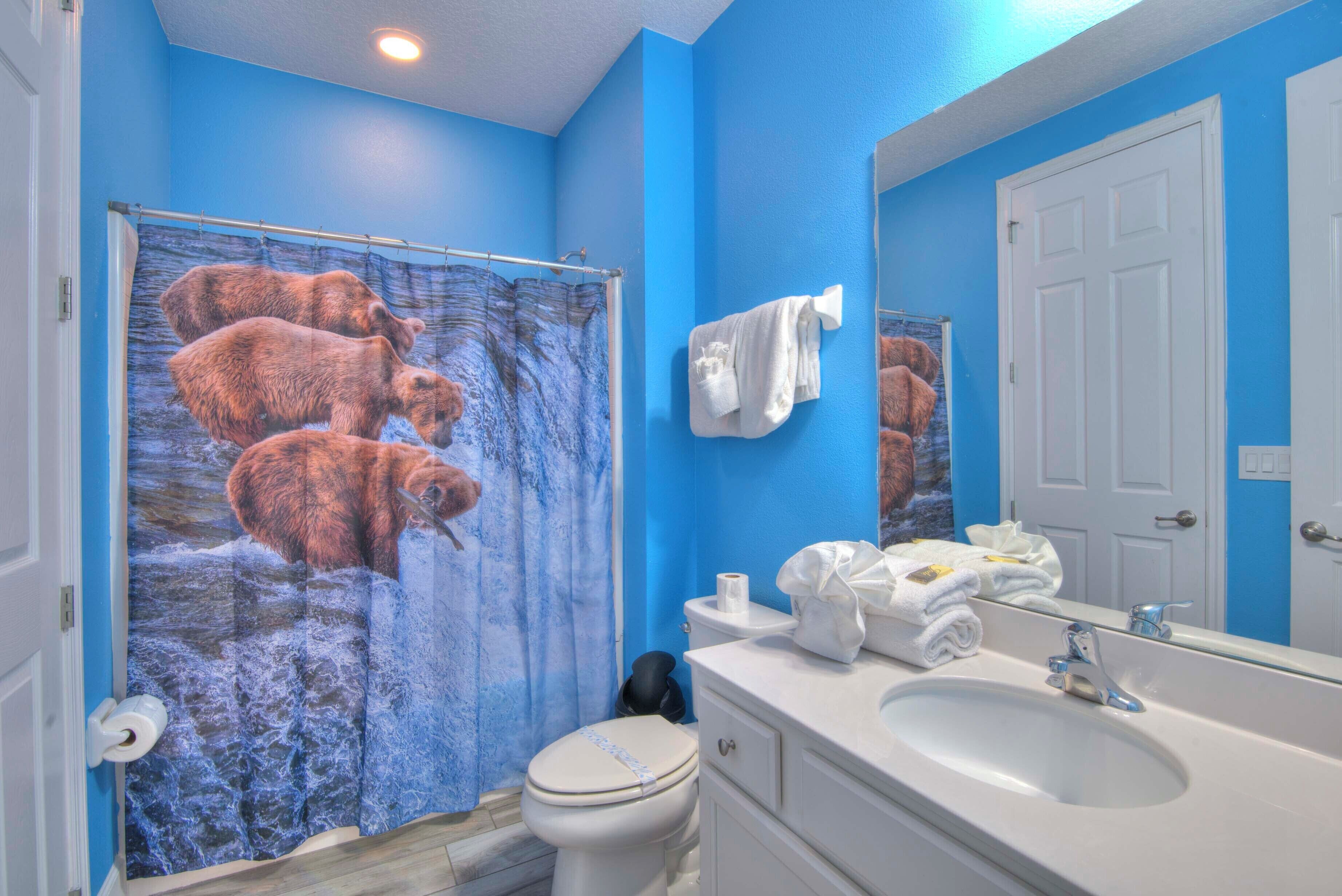 Un baño con pared azul, lavamanos blanco, inodoro y cortina de ducha con osos.
