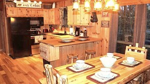 A cabin-style kitchen with wooden cabinets, a central island, and a dining area with stools. - MOUNTAIN TOP Lodge with Gorgeous Panoramic View, Hot Tub, Pool Table & Fireplace (Sevierville)