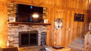 A cozy living room with a stone fireplace, a flat-screen TV mounted above it, and a mounted animal head decoration. - MOUNTAIN TOP Lodge with Gorgeous Panoramic View, Hot Tub, Pool Table & Fireplace (Sevierville)