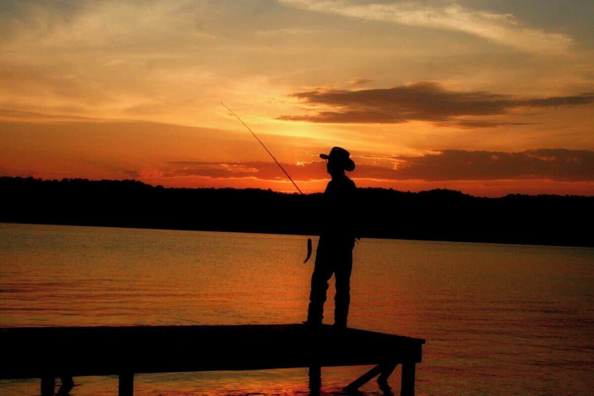 A silhouette of a person fishing at sunset.