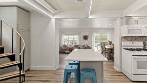 A modern kitchen with white appliances, a central island with stools, and a staircase with black railings. - Always East Lake-  all sports lake, on Little Hart Lake, swim, kayak, fishing (Twin Lake)