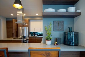 Une cuisine moderne dotée d’un îlot central, d’appareils électroménagers en acier inoxydable, de meubles en bois et d’une plante décorative.