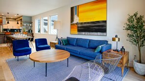 Una sala moderna con un sofá azul, una mesa de centro redonda de madera y un comedor con mesa preparada para cuatro personas.