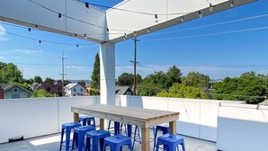 Un patio al aire libre con una mesa de madera y taburetes azules, rodeado de paredes blancas y luces colgantes.