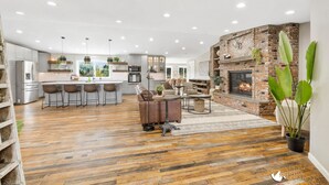 A spacious living area with a kitchen, a fireplace, and a dining area. - 3 Acres Remodeled Home With Hot Tub Walking Distance to Beach! Garden & Fire Pit (Coeur d Alene)