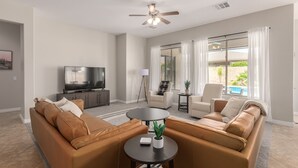 Un salon moderne comprenant un ensemble de canapés, un téléviseur, un ventilateur de plafond et une vue sur une piscine.