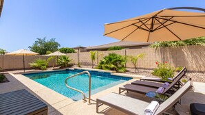 Un jardin avec une piscine, des chaises longues et des parasols.