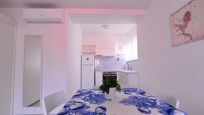 Un espace de vie compact comprenant un coin repas, une kitchenette et une petite table à manger recouverte d’une nappe bleue.