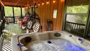 Een hottub op een houten terras, met een hangstoel en uitzicht op bomen.
