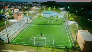 Ein Sportplatz mit Netz, umgeben von einem Zaun, mit Gebäuden im Hintergrund.