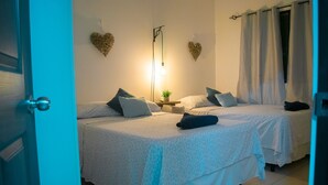 Ein Schlafzimmer mit zwei Betten, einem Nachttisch mit Lampe und dekorativer Wandkunst in Herzform.