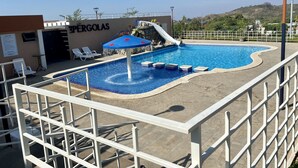 Ein Swimmingpool mit Rutsche, Liegestühlen und einer Pergola.