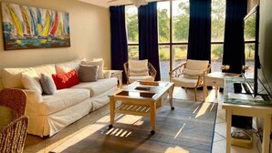 Uma sala de estar com sofá, cadeiras, mesa de centro e um quadro na parede.