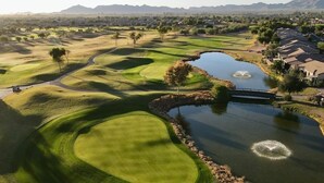 Un parcours de golf avec un étang, un pont et des immeubles résidentiels en arrière-plan.