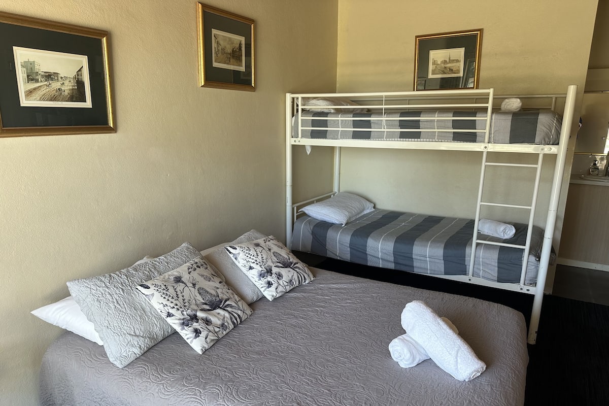 A bunk bed room with a grey patterned bedspread, two pillows with floral designs, and a rolled white towel.