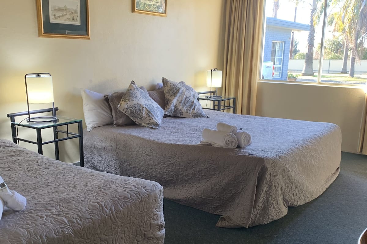 A hotel room with two beds, a nightstand with a lamp, and a window with curtains.