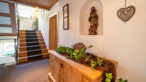 Een houten trap die naar een deur leidt, een beeld aan de muur en een houten kast met planten.