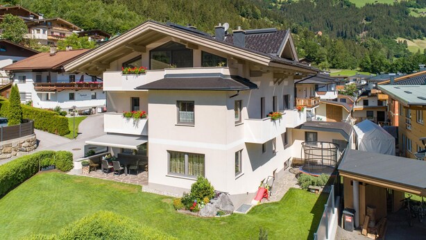 Een modern huis met twee verdiepingen en een balkon, omgeven door weelderige begroeiing en een bergachtig landschap.