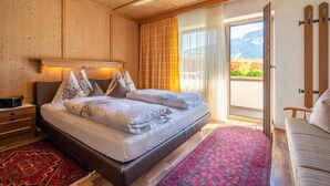 Een slaapkamer met houten lambrisering, een bed, een nachtkastje, een tapijt met een rood patroon en uitzicht op bergen door een raam.