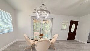 Ein Essbereich mit einem Glastisch, vier Stühlen, einer Chandelierleuchtre und einer Tür mit einer dekorativen Glasscheibe.