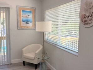 Um quarto com uma poltrona branca, luminária de chão, quadro emoldurado e janela com persianas.