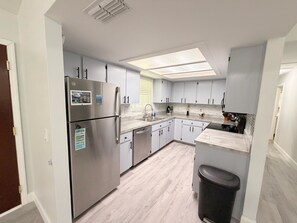 A modern kitchen with a stainless steel refrigerator, white cabinets, a skylight, and a black trash bin.