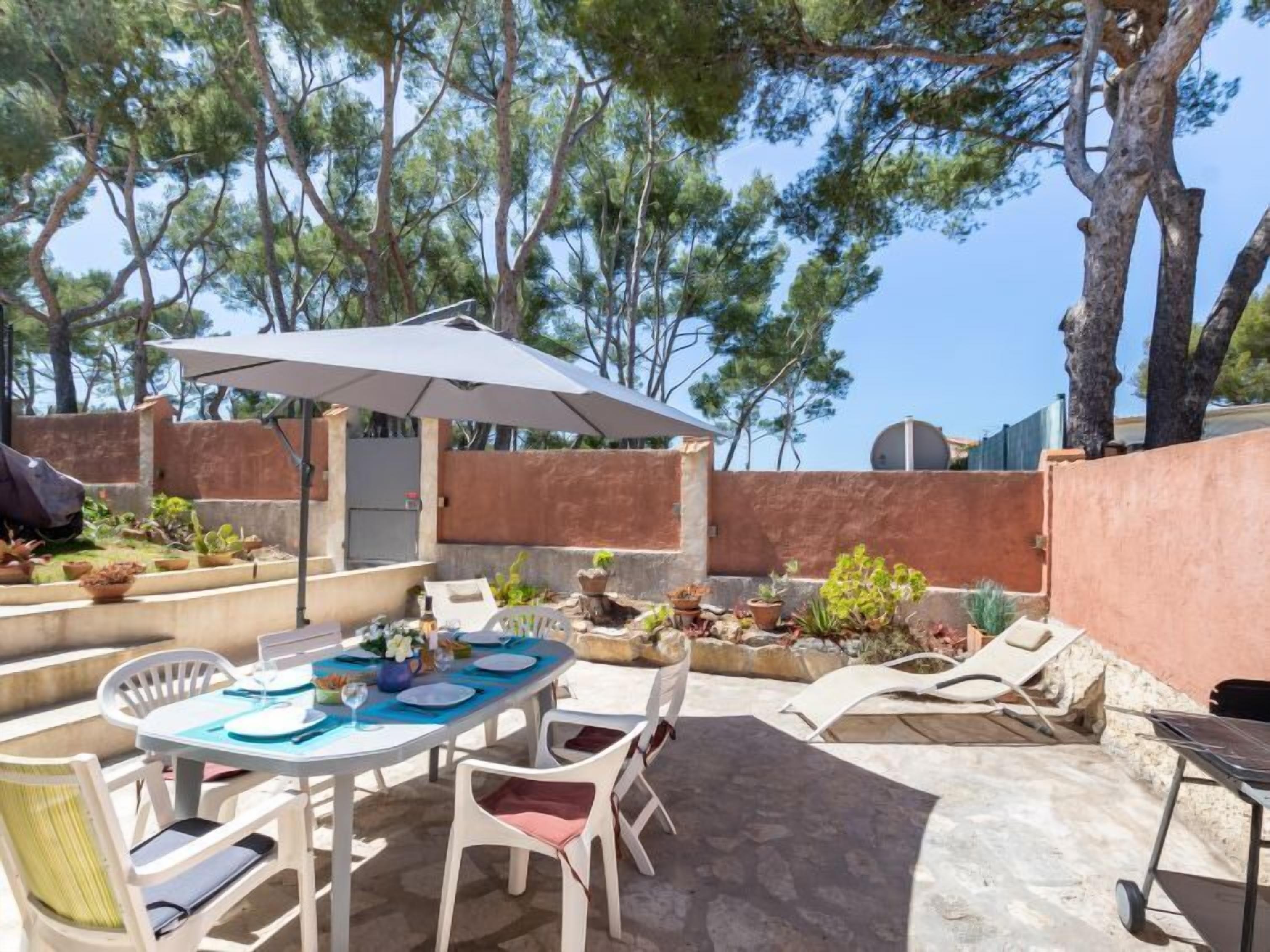 An outdoor patio with a table set for dining, surrounded by potted plants and a large umbrella.