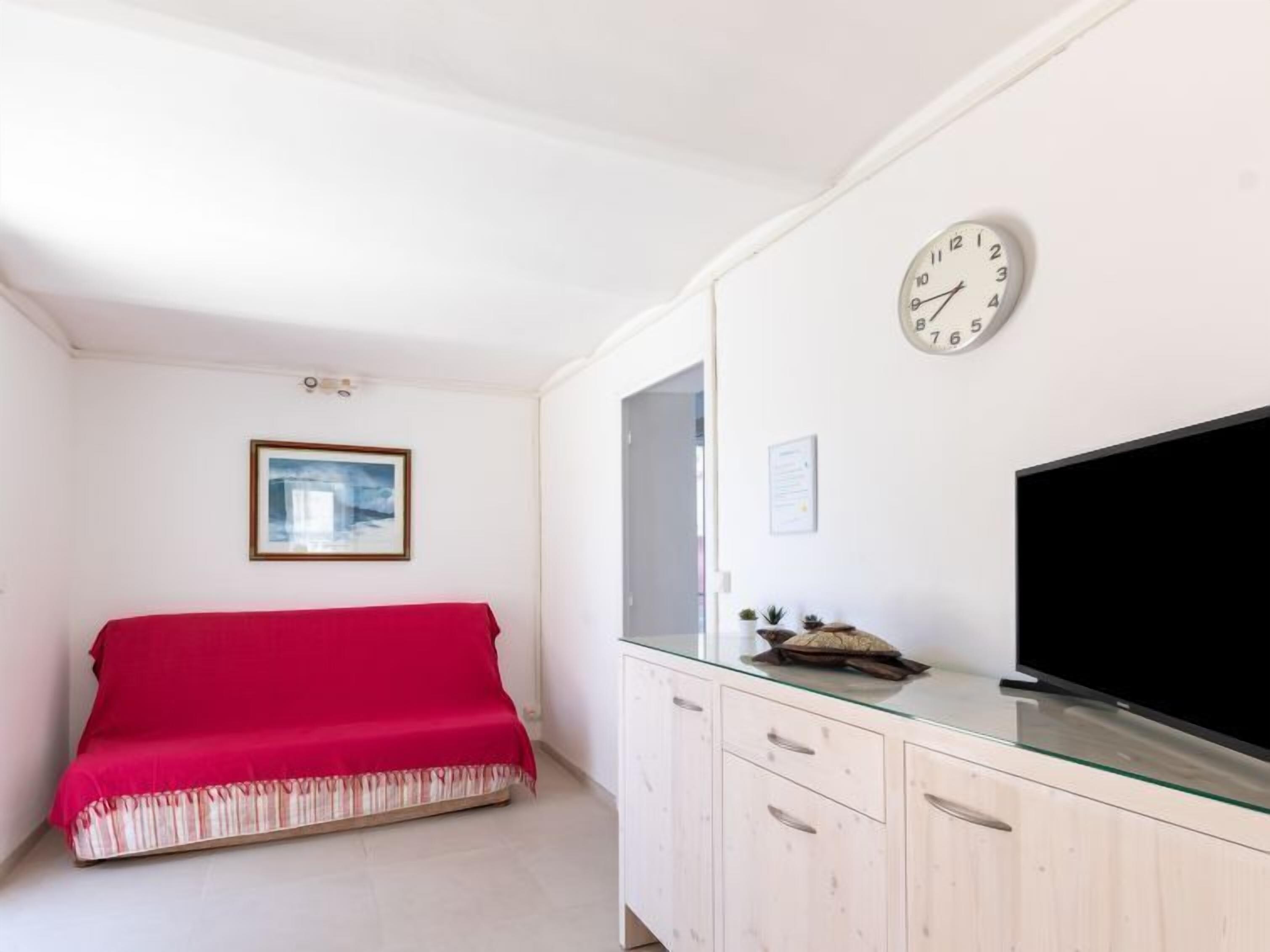 A bedroom with a bed, a TV, a clock, and a framed picture on the wall.
