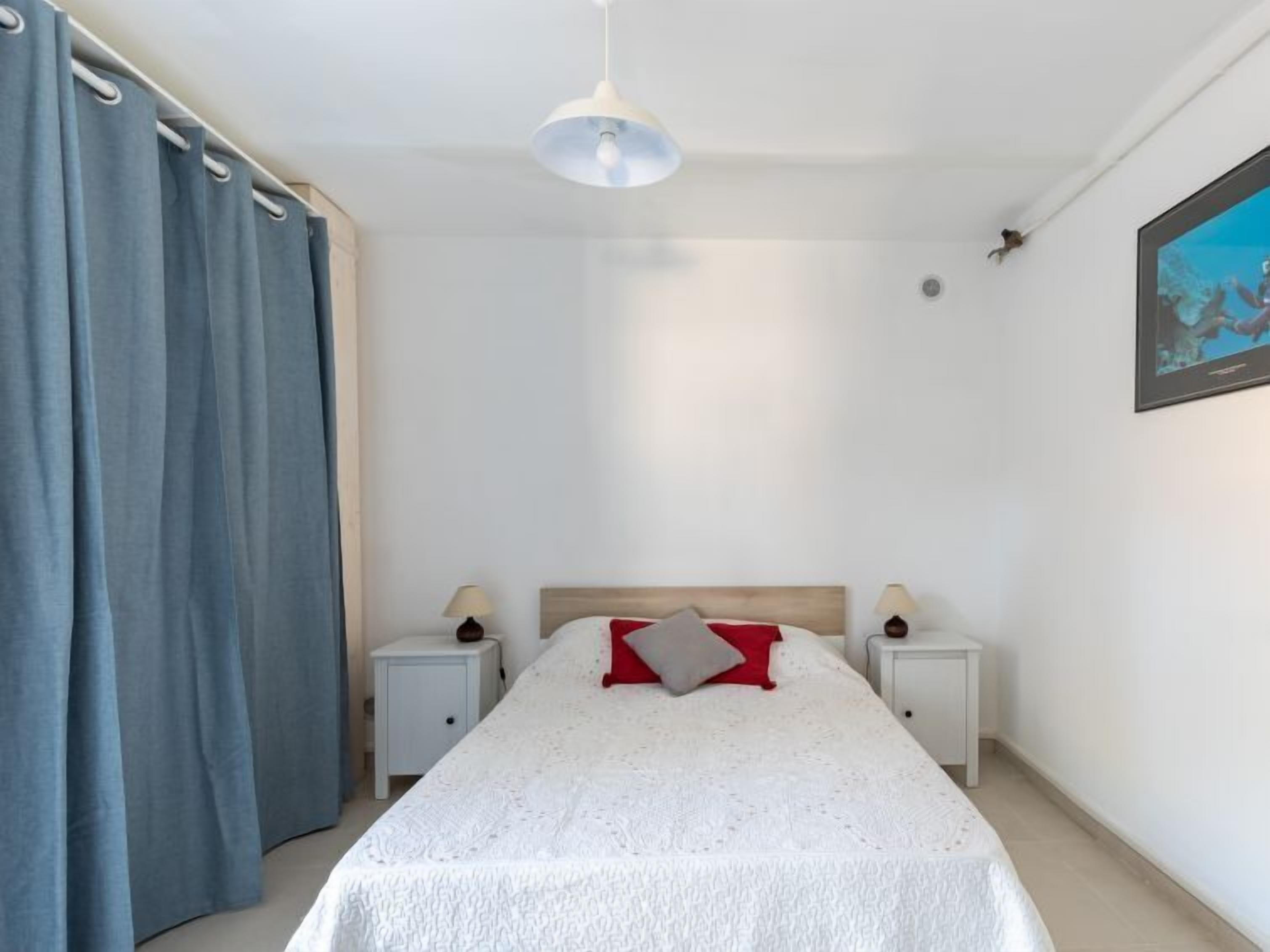 A bedroom with a single bed, two bedside tables, a ceiling light, and a painting on the wall.