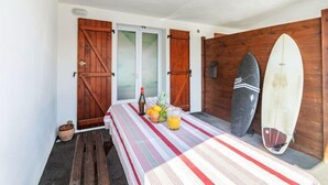 Ein Zimmer mit einem Bett, einem Tisch mit Obst und Getränken, Holztüren und zwei Surfbrettern.