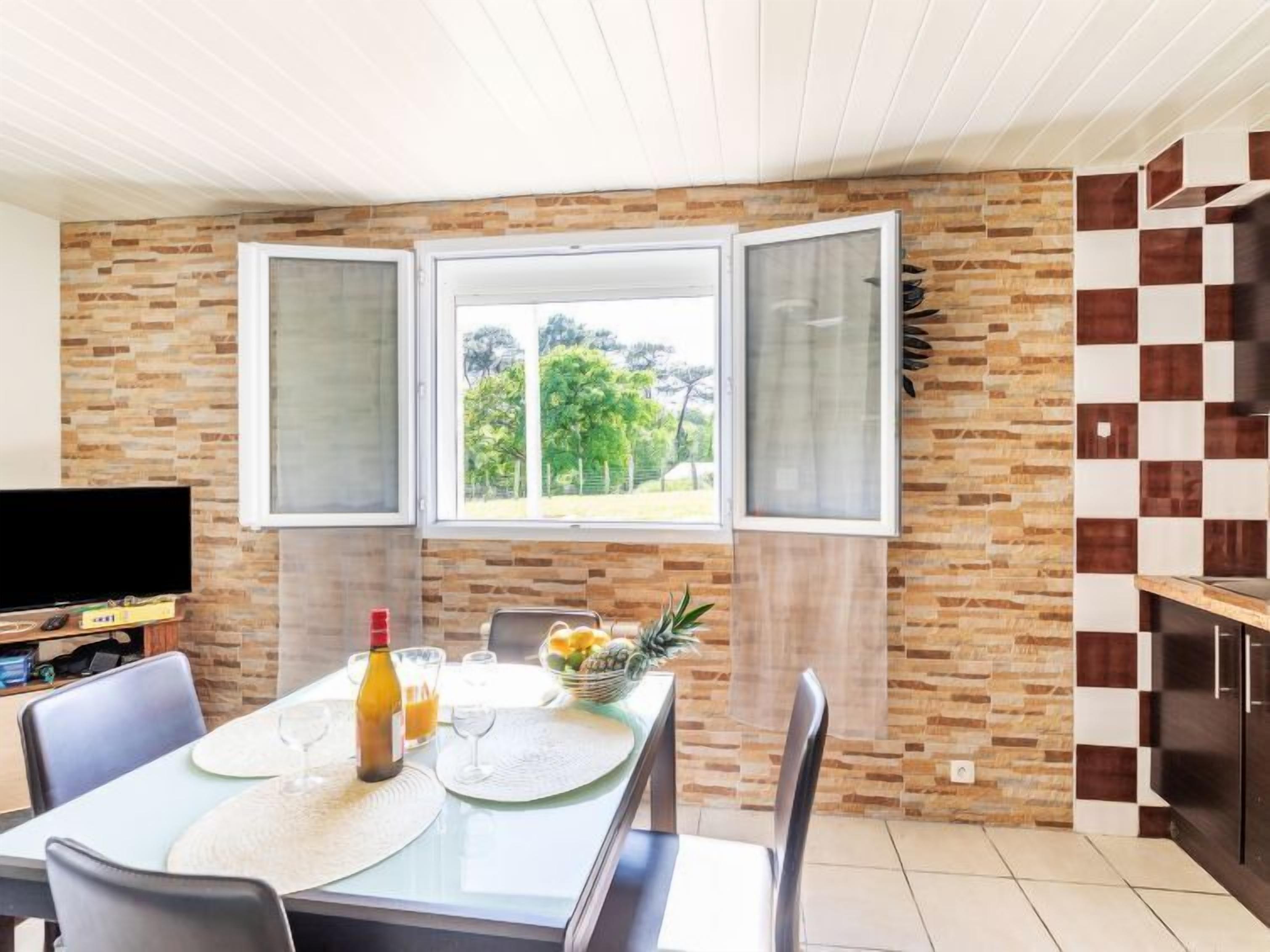 A dining area with a table set for two, a TV, and a window with a view of greenery.