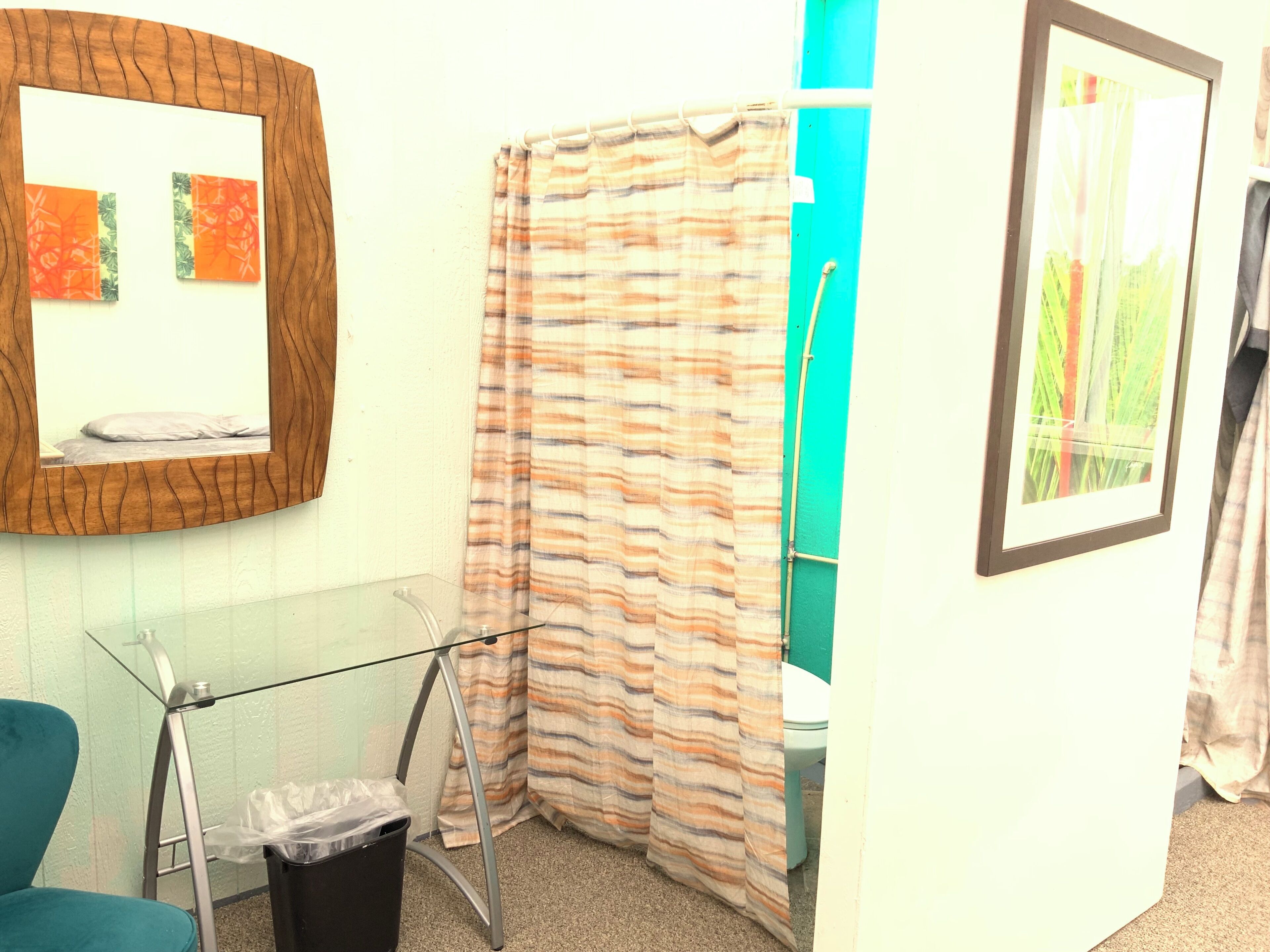 Un baño con cabina de ducha de vidrio, inodoro, cubo de basura y espejo con obra de arte.