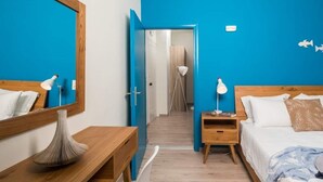 Habitación de hotel con cama de madera, mesita de noche, espejo y una pared azul de acento.