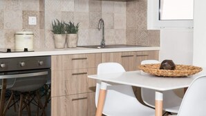 Cocina moderna con armarios de madera, pileta de acero inoxidable y encimera blanca. Hay una estufa, una pequeña planta y una cesta con un objeto marrón en la encimera.