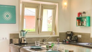 Cozinha com área de refeições, janela, prateleira verde com utensílios de cozinha e luminária na parede.