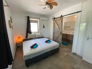 Ein Schlafzimmer mit Bett, Deckenventilator, Nachttisch mit Lampe und einer Schiebetür zum Badezimmer.