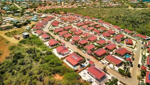 Um bairro residencial com várias casas de telhado vermelho dispostas em um padrão de grade, cercado por vegetação e uma orla costeira.
