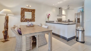 Una cocina moderna con una isla central, una zona de comedor con mobiliario de mimbre y un espejo grande con marco de madera.