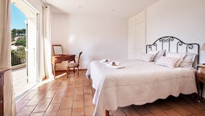 A bedroom with a large bed, a wooden chair, a desk, and a view of the outside.