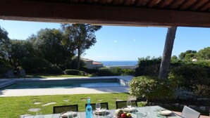 A dining table set outdoors with a view of a swimming pool and ocean.