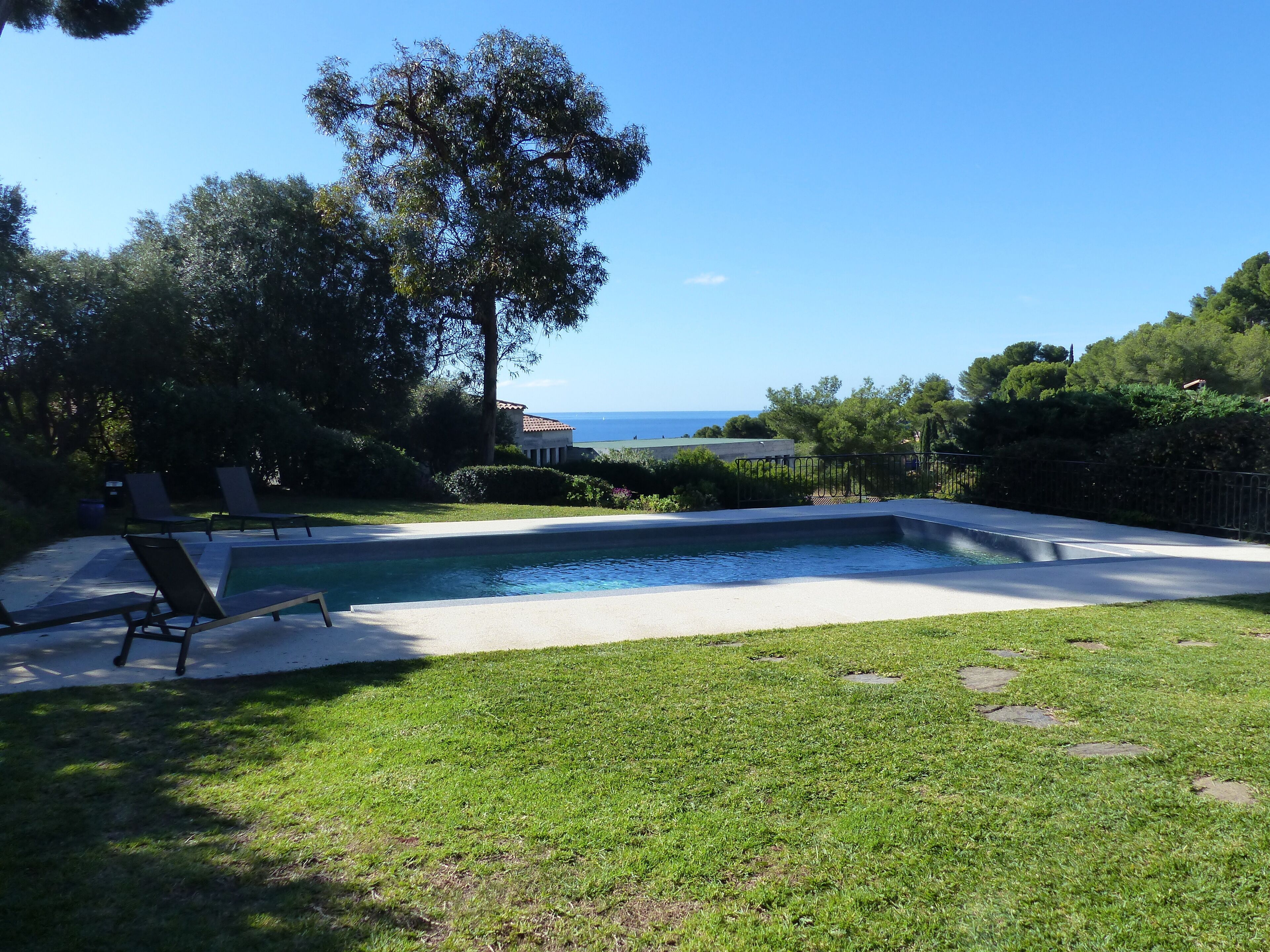 Piscina com espreguiçadeiras, área gramada e vista para o mar.