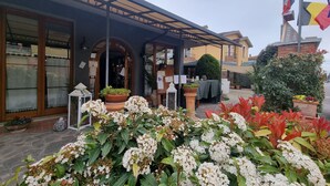 L'entrée d'un hôtel, avec un patio couvert, des plantes en pot et des drapeaux.