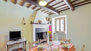 Un coin repas avec une table dressée pour quatre personnes, une cheminée, un téléviseur posé sur une table d’appoint et une fenêtre donnant sur un beau paysage.