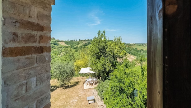 Une vue depuis une fenêtre donnant sur un paysage rural, avec un petit bâtiment blanc et une table entourée de chaises.