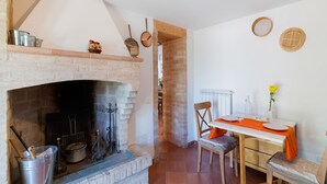 A rustic kitchen with a brick fireplace, wooden shelves, and a dining area with a table and chairs.